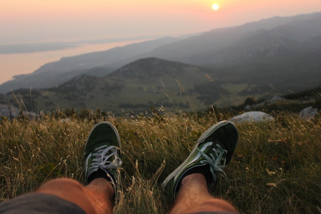 Feet in green sneakers overlooking coastal sunset