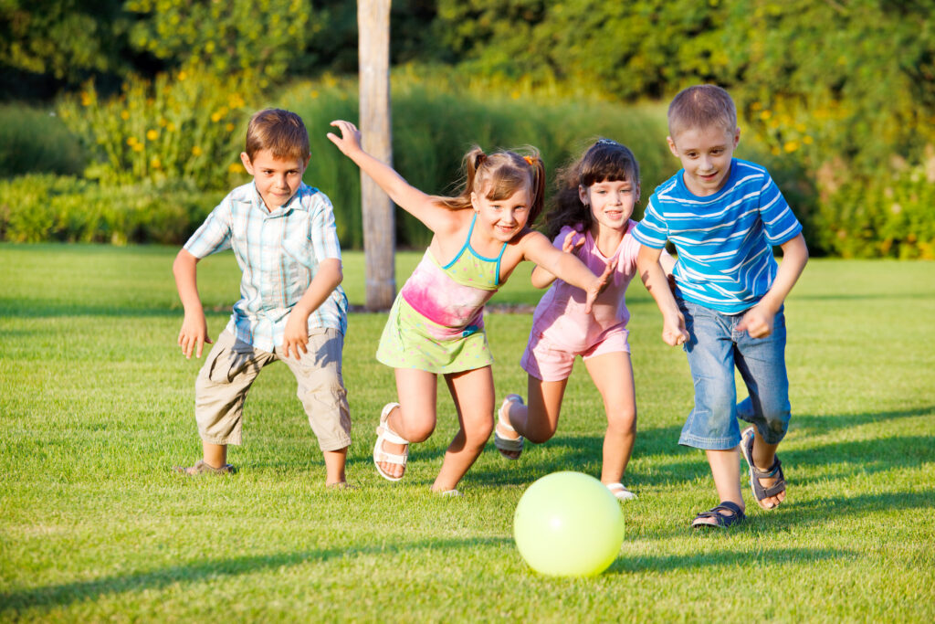 Four children chasing ball on green lawn