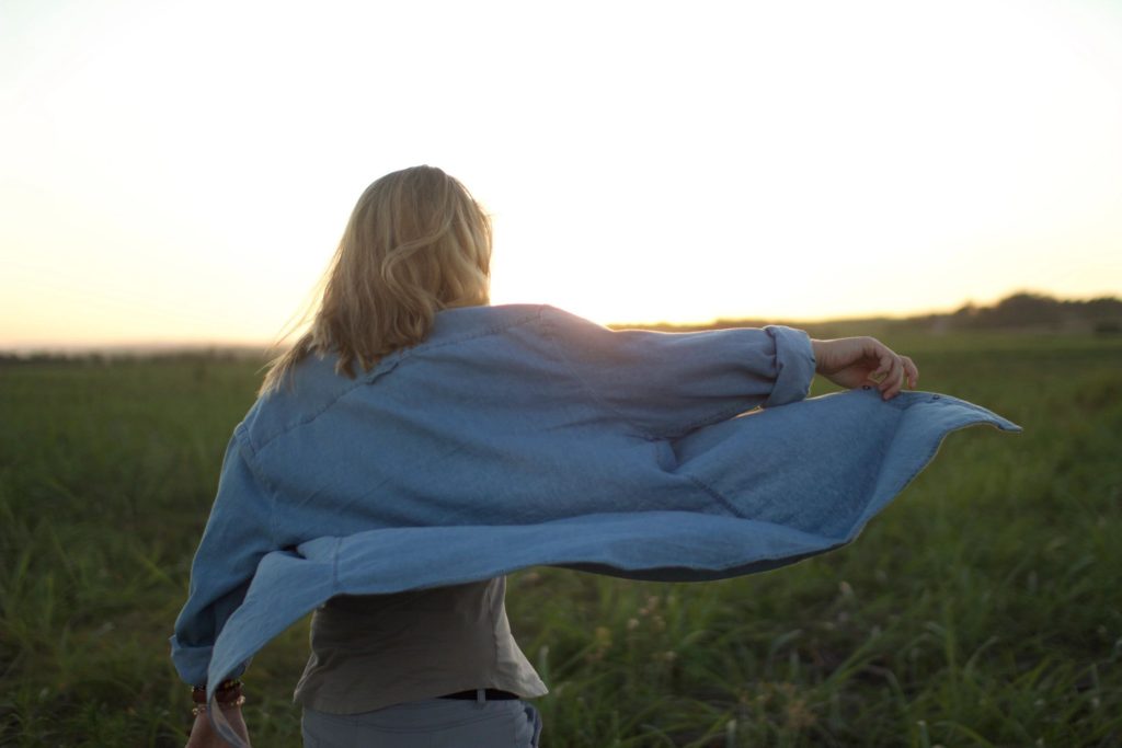 Person twirling in grassy field at sunset