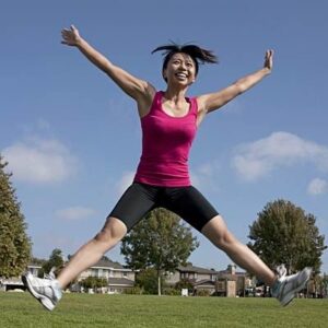 Woman doing a plyo-jack with a big smile in the park