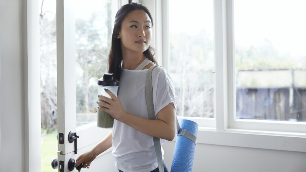 Woman with yoga mat opening glass door.
