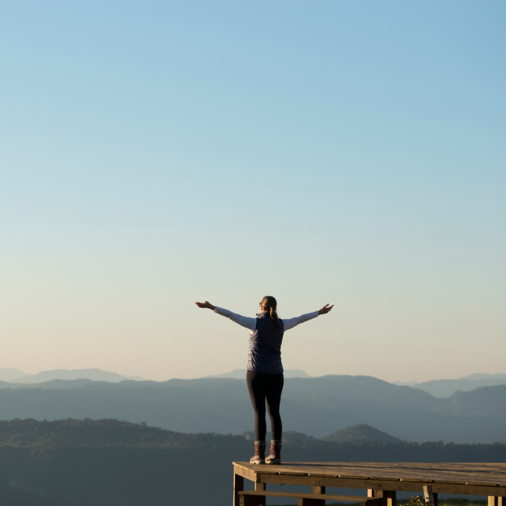 Person standing on platform, arms outstretched, mountains