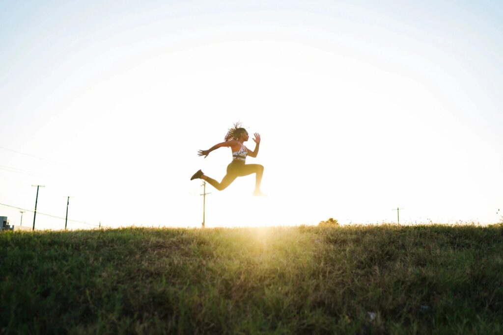 Person jumping over grassy hill at sunrise
