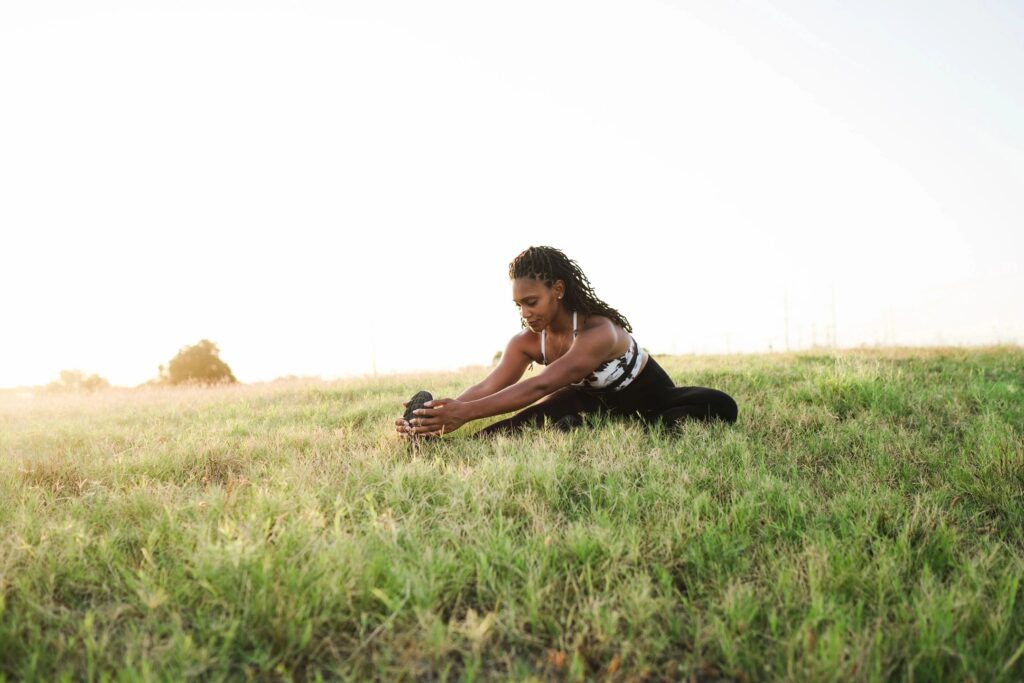 Woman doing seated hamstring stretch in field.