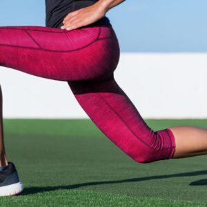 Woman in magenta leggings doing a lunge on turf or grass