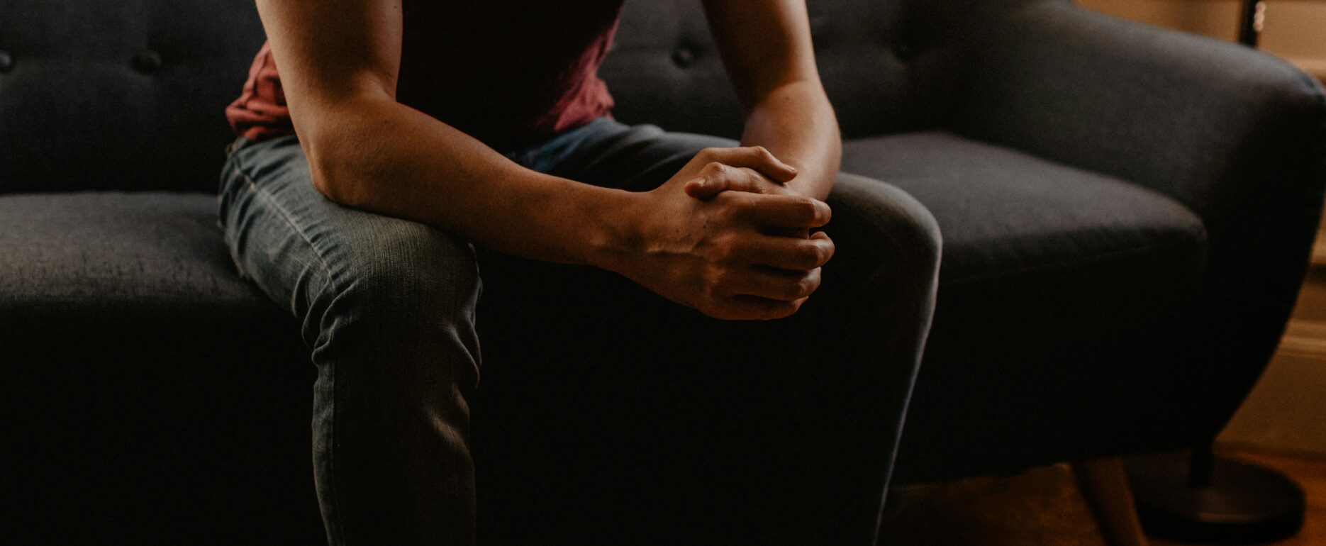 Man sitting on coach with hands clasped on knees