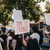 Time for Change and Silence is Violence protestor signs with people marching in street during the summertime.