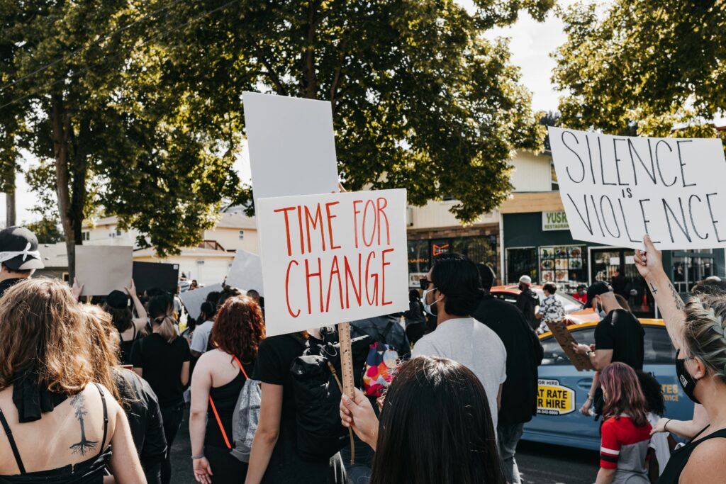 Time for Change and Silence is Violence protestor signs with people marching in street during the summertime.