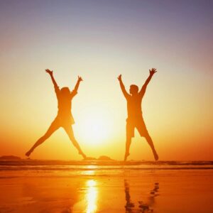two people jumping on beach in sunset